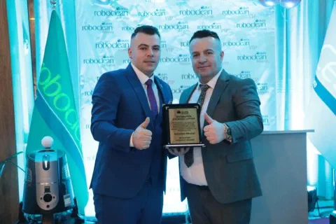 Two participants with a plaque before a Roboclean backdrop